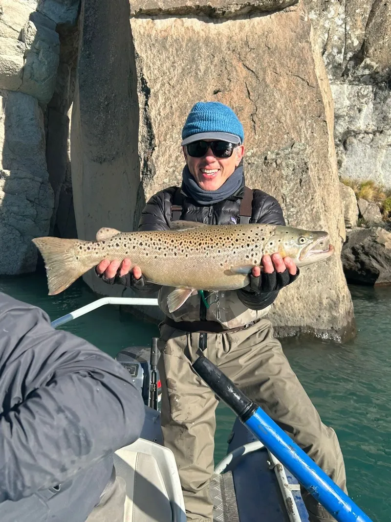 Pescador sonriente sostiene una gran trucha marrón capturada con mosca en el lago General Carrera, Aysén, Patagonia chilena