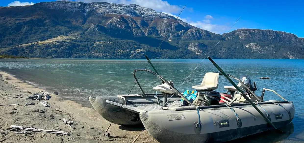 Two fishing catarafts beached on the shore of a Patagonian lake below snow-dusted mountains