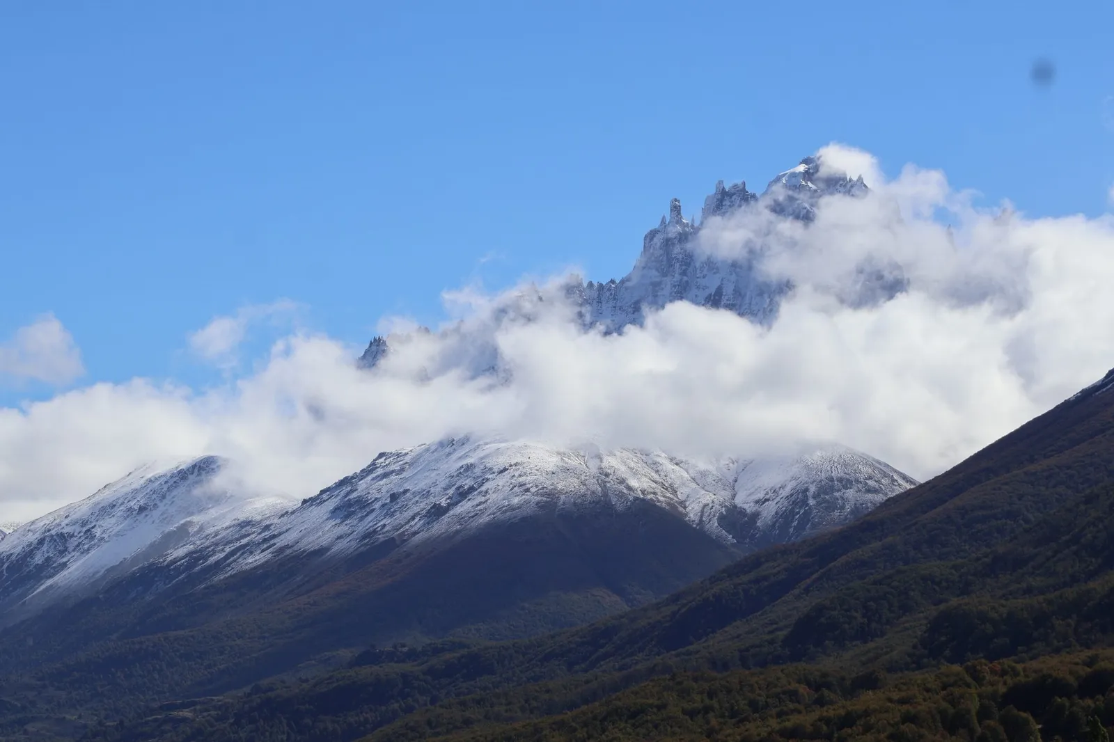 Cumbres nevadas del Cerro Castillo entre nubes, sobre bosque otoñal en Aysén, Patagonia chilena