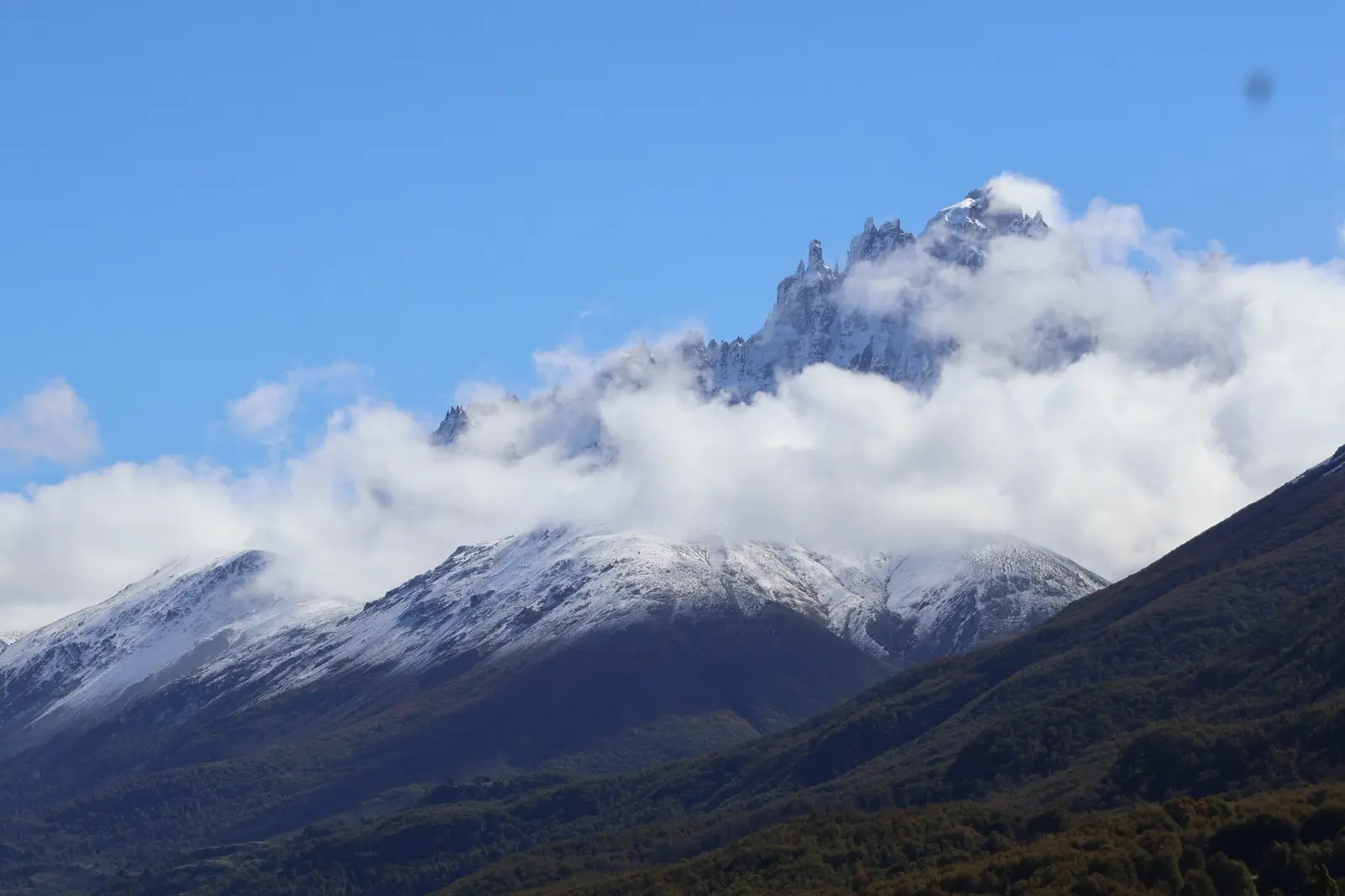 Cumbres nevadas del Cerro Castillo entre nubes, sobre bosque otoñal en Aysén, Patagonia chilena