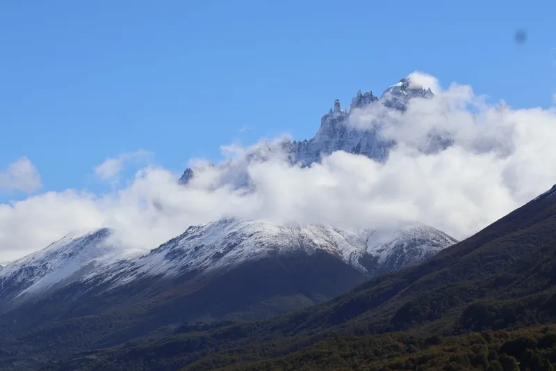 Cumbres nevadas del Cerro Castillo entre nubes, sobre bosque otoñal en Aysén, Patagonia chilena