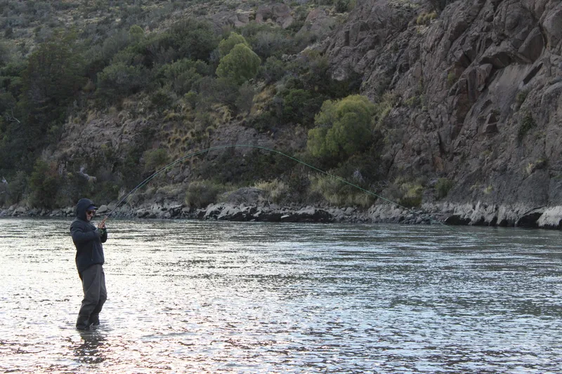 Pescador con mosca peleando un pez con la caña curvada en un río de Aysén, Patagonia chilena