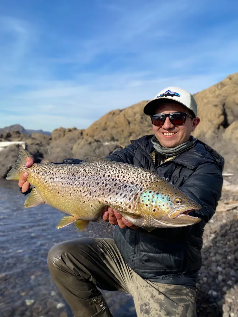 Pescador sostiene una gran trucha marrón a orillas de un lago en Chile, Patagonia chilena