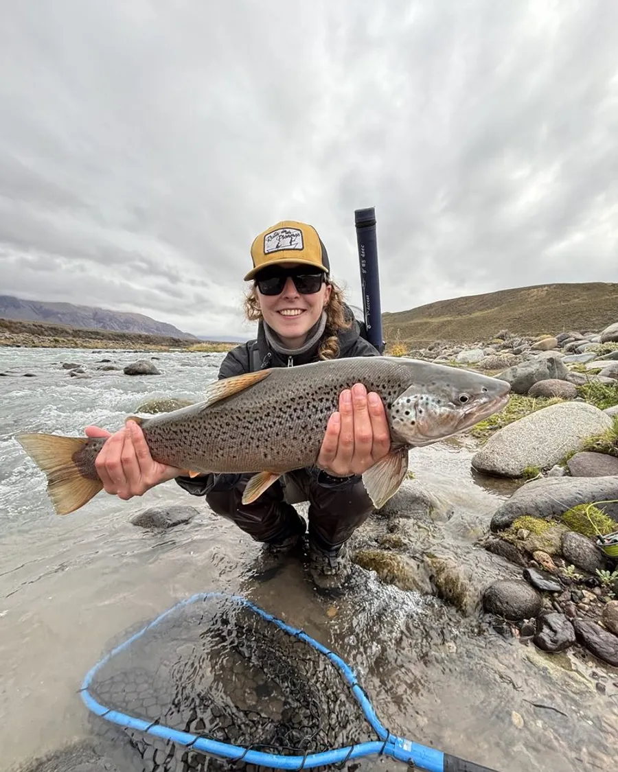 Angler holding a large brown trout beside a river in Chilean Patagonia